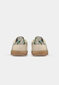 Sapatilhas com padrão floral, corpo em lona creme, detalhes florais azuis e sola de borracha texturizada castanha. Atacadores planos e design de cano baixo.