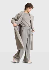 Sivi vuneni kaput preko sivoj majice dugih rukava i širokih jogger hlača. Outfit ima pojas s vezicom i mekan, udoban materijal. Ležerne tenisice.
