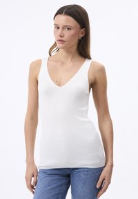 Valge ribaga tank top V-kaelusega ja laiad rihmad, keha lähedane disain ja sile tekstuur, kombineeritud siniste teksadega.
