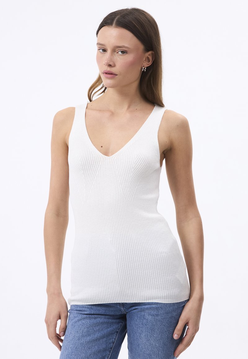 Valge ribaga tank top V-kaelusega ja laiad rihmad, keha lähedane disain ja sile tekstuur, kombineeritud siniste teksadega.