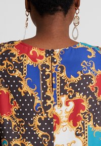 Flerfärgad blus med utsmyckade guldmönster, prickar och knappstängning i ryggen. Tillverkad av mjukt tyg med en avslappnad passform.