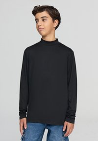 Czarna bluzka z długim rękawem i golfem, wykonana z gładkiej tkaniny, o dopasowanym fasonie i wysokim kołnierzu, zestawiona z niebieskimi spodniami dżinsowymi.