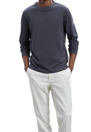 Czarny bawełnowy t-shirt z długimi rękawami i okrągłym dekoltem, o gładkiej fakturze, z białymi paskami akcentującymi na lewym rękawie. W połączeniu z białymi spodniami.