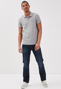 Polo gris de manga corta con cuello, que cuenta con un bolsillo, combinado con jeans azul oscuro y zapatillas blancas. Atuendo simple y casual.