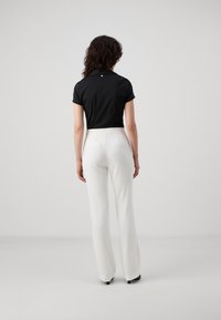 Polo shirt nero a maniche corte, vista posteriore, abbinato a pantaloni bianchi a gamba larga. Tessuto liscio, design minimalista e piccolo logo dettagliato sul collo.
