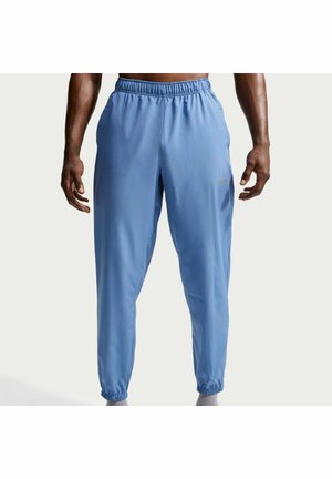 Modèle masculin portant un pantalon de jogging bleu clair avec taille élastique et poignets aux chevilles sur un fond uni.