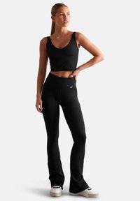 Zwarte geribde crop top en hooggetailleerde flared leggings, met een soepele textuur en minimalistisch ontwerp, gecombineerd met witte sportschoenen.