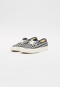Mustat ja valkoiset houndstooth-kuvioidut lenkkarit, joissa on kangasyläosa, valkoinen kumipohja ja kermanväriset nauhat. Pyöreä kärki ja matala malli.