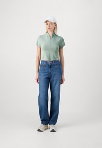 Top corto de color verde claro con cremallera y mangas cortas; vaqueros anchos azules; gorra de béisbol blanca; zapatillas grises y blancas.