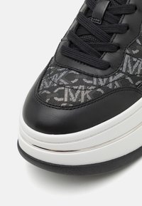 Černé tenisky s texturovaným svrškem s vzorovaným designem, solidními černými koženými prvky a silnou bílou mezipodešví se stříbrnými akcenty.