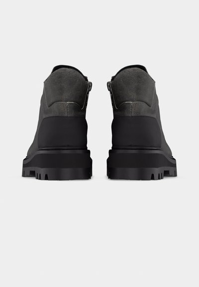 Ζευγάρι από σκούρα γκρι και μαύρες ανθεκτικές μπότες, εμφανιζόμενες από πίσω σε απλό φωτεινό φόντο.