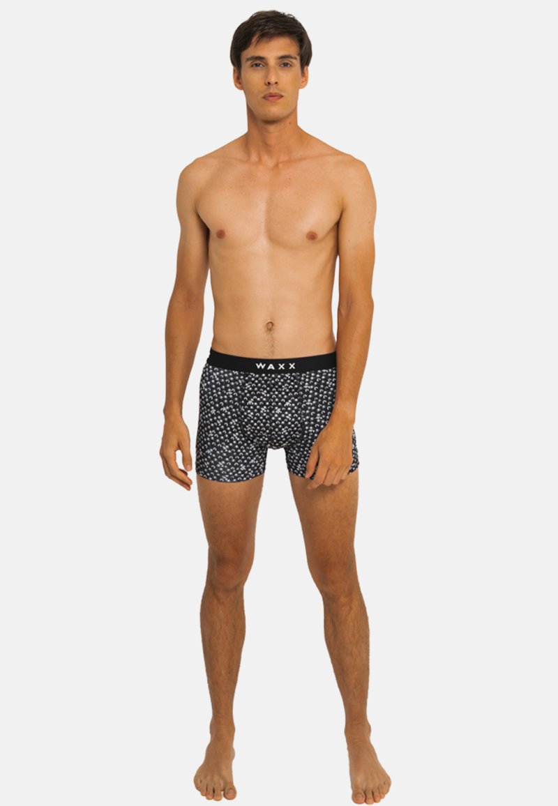 Boxer-briefs noirs avec des motifs abstraits blancs et une ceinture élastique douce portant l'inscription "WAXX." Fabriqués en tissu extensible pour le confort.