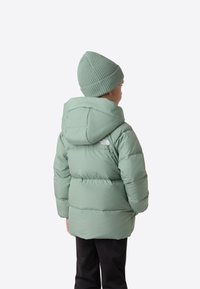 Grøn polstret jakke med hætte og logo på ryggen, kombineret med en lysegrøn ribstrikket hue, båret af et barn.