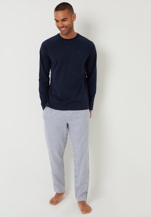 Granatowa koszulka z długim rękawem, z okrągłym dekoltem i fakturą rib, w zestawie z niebieskimi i białymi spodniami do piżamy w paski. Oba elementy wykonane są z lekkiej bawełny.