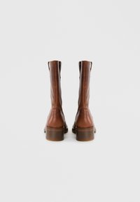 Bottines en cuir marron avec une texture lisse, un talon bas et des tirettes à l'arrière, présentant un design épuré et sans motifs visibles.