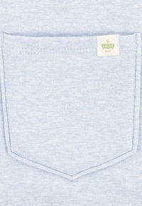 Tela de algodón azul claro con un bolsillo en el pecho que presenta una etiqueta blanca que dice "Levi's Baby". Superficie texturizada con un sutil patrón jaspeado.