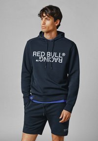 Sudadera navy con texto blanco "RED BULL RACING", cordón ajustable y mangas largas, combinada con pantalones cortos navy a juego.