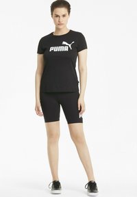Camiseta deportiva negra con el logo blanco de "PUMA", combinada con shorts ajustados negros que también tienen el logo, ambos hechos de una tela suave. Zapatillas negras.