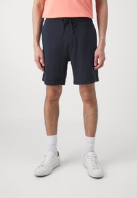 Tamsiai mėlynos sportinės šortai su elastinga juosta ir šnaru, su paprastu dizainu ir šiek tiek laisvu kirpimu. Baltos sportbačiai ir kojinės.