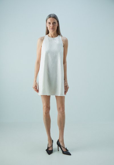 Robe sans manches blanche ornée de sequins, à coupe décontractée, associée à des escarpins noirs à bout pointu. Texture lisse et design minimaliste.