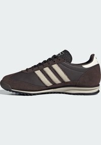 Tamno smeđi Adidas tenisice s bež potpisom od tri pruge, teksturiranom kožom i panelima od velura, crnim vezicama i rebrastim potplatom.