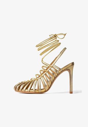 Goldener High-Heel-Sandal mit strappy Design, ausgestattet mit dünnen, metallischen Riemen und einem schlanken Stiletto-Absatz. Glatte, reflektierende Textur.