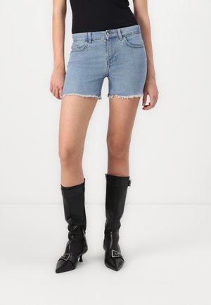 Shorts en denim bleu clair avec un ourlet effiloché, associés à des bottes noires montantes à bout pointu et avec un accent de boucle.