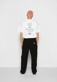 Biała koszulka z nadrukiem z czarnym tekstem i wzorami na plecach, połączona z czarnymi spodniami. Do stroju dopasowano ciemne buty.