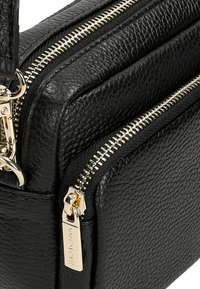 Černá texturová kožená taška se zlatými zipy. Obsahuje dvě přihrádky a značený zipový ucho. Akcentovaná kovová část dodává detail.