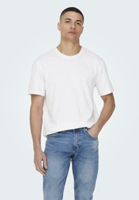 White cotton t-shirt with short sleeves, crew neckline, relaxed fit, worn with blue denim jeans featuring a classic straight-leg cut.