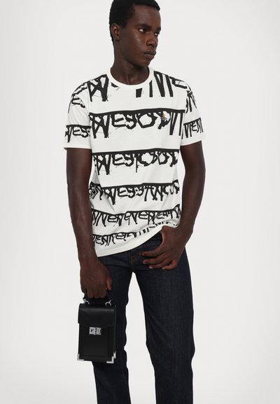 Weißes T-Shirt mit fettem schwarzen Textmuster, ergänzt durch eine bunte Grafik. Kombiniert mit dunklen Jeans und einer kleinen schwarzen Handtasche.