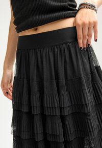 Jupe noire à volants avec une large taille élastique et plusieurs couches froncées composées d'un mélange de matériaux texturés et transparents.