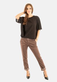 Top negro de manga corta con un acabado texturizado, combinado con pantalones marrones remangados y tacones altos negros. Diseño de outfit simple y moderno.