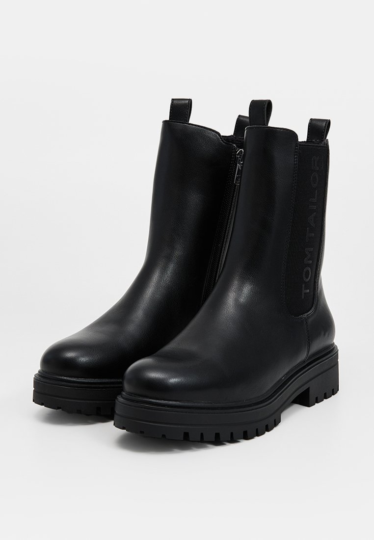 Bottines en cuir noir avec une texture lisse, des panneaux latéraux élastiques et une semelle en caoutchouc épaisse. Présente un logo sur le côté pour le branding.