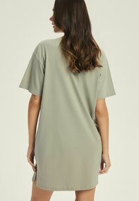 Oliwkowa, oversize sukienka t-shirtowa z krótkimi rękawami i zaokrąglonym dołem. Wykonana z miękkiej bawełny, o luźnym kroju i bocznych rozporkach.