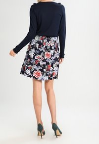 Navy long-sleeve top paired with a floral patterned skirt featuring red and white flowers on a dark background, completed with green high heels.