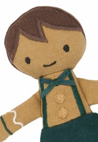 Gestrickte Puppe mit beige-farbenem Gesicht, braunen Haaren, grünen Hosenträgern und einem gemusterten Hemd. Hat ein lächelndes Gesicht und gestickte Details.