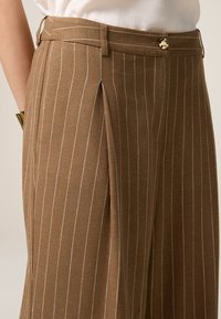 Bruna randiga byxor i lättviktsmaterial, med skräddarsydd passform, framfickor och en metallknapp som stängning i midjan.
