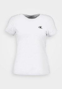 Vit bomulls t-shirt med korta ärmar, rundad halsringning och ett subtilt mönster; har en liten svart "ck"-logotyp på vänster bröst.
