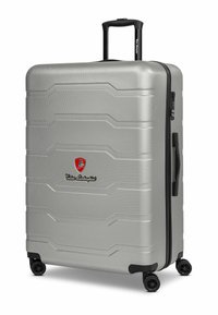 Maleta rígida plateada con acabado texturizado, que cuenta con cremallera negra, asa y cuatro ruedas giratorias. Logo exhibido de forma prominente.