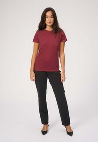 Bordeaux kortærmet t-shirt kombineret med sorte lige ben bukser og sorte spidse hæle, sat mod en hvid baggrund.