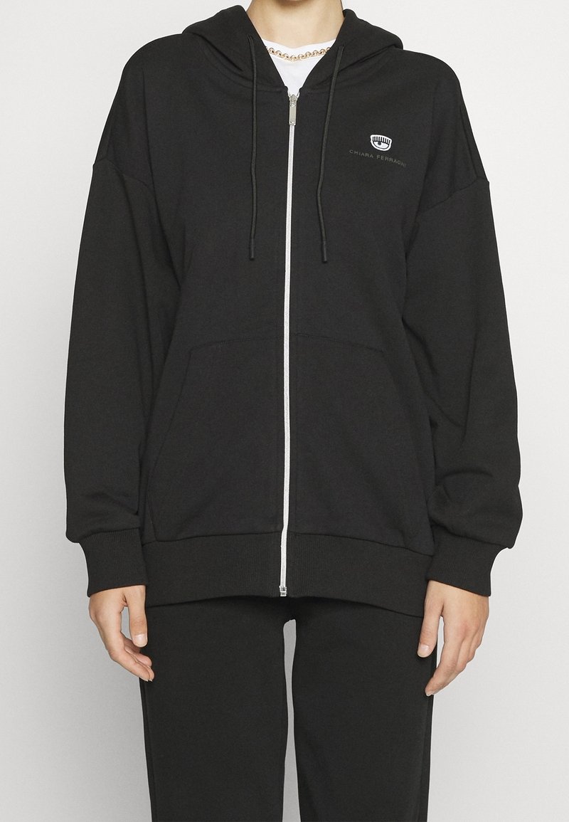 Mustapohjainen vetoketjullinen huppari, valmistettu pehmeästä kankaasta, jossa on huppu, etutaskut ja resorit hihansuissa. Vasemmassa rintakehässä pieni harmaa logo.