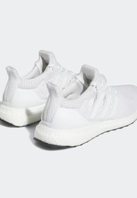 Vitaidna sportskor i vitt med en texturerad mesh-ovandel, tre vita ränder och en dämpad Boost-sula. Har en slät gummiyttersula.