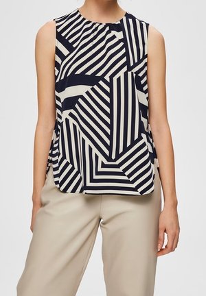 Sleeveless top with black and white geometric stripe patterns paired with beige high-waist trousers on a standing person.