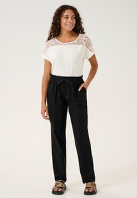 Maglietta bianca con colletto in pizzo e maniche corte abbinata a pantaloni neri con cordoncino, dotati di tasche laterali e una silhouette a gamba larga.