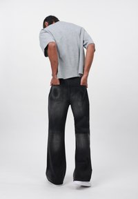 Camiseta gris de manga corta combinada con pantalones vaqueros de pierna ancha negros, que cuentan con dos bolsillos traseros y un acabado desgastado, usados con zapatillas blancas.