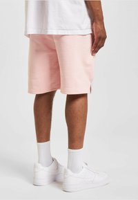 Shorts en coton rose avec des fentes sur les côtés, associés à des chaussures de sport blanches et des chaussettes blanches côtelées, visibles de l'arrière.
