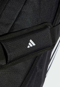 Musta reppu, jossa on teksturoitu pinta, valkoisella Adidas-logolla ja useilla hihnoilla. Sisältää erilaisia geometrisia kuvioita ja yksityiskohtia.
