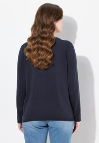 Marineblaue Langarmbluse mit Rundhalsausschnitt und gerippten Bündchen, getragen über hellblauen Jeans, die eine glatte Textur und ein minimales Design zeigen.