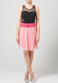 Top in rete nera con scollatura a cuore, abbinato a una gonna rosa con vita alta e tre bottoni neri. Tacchi alti argentati.